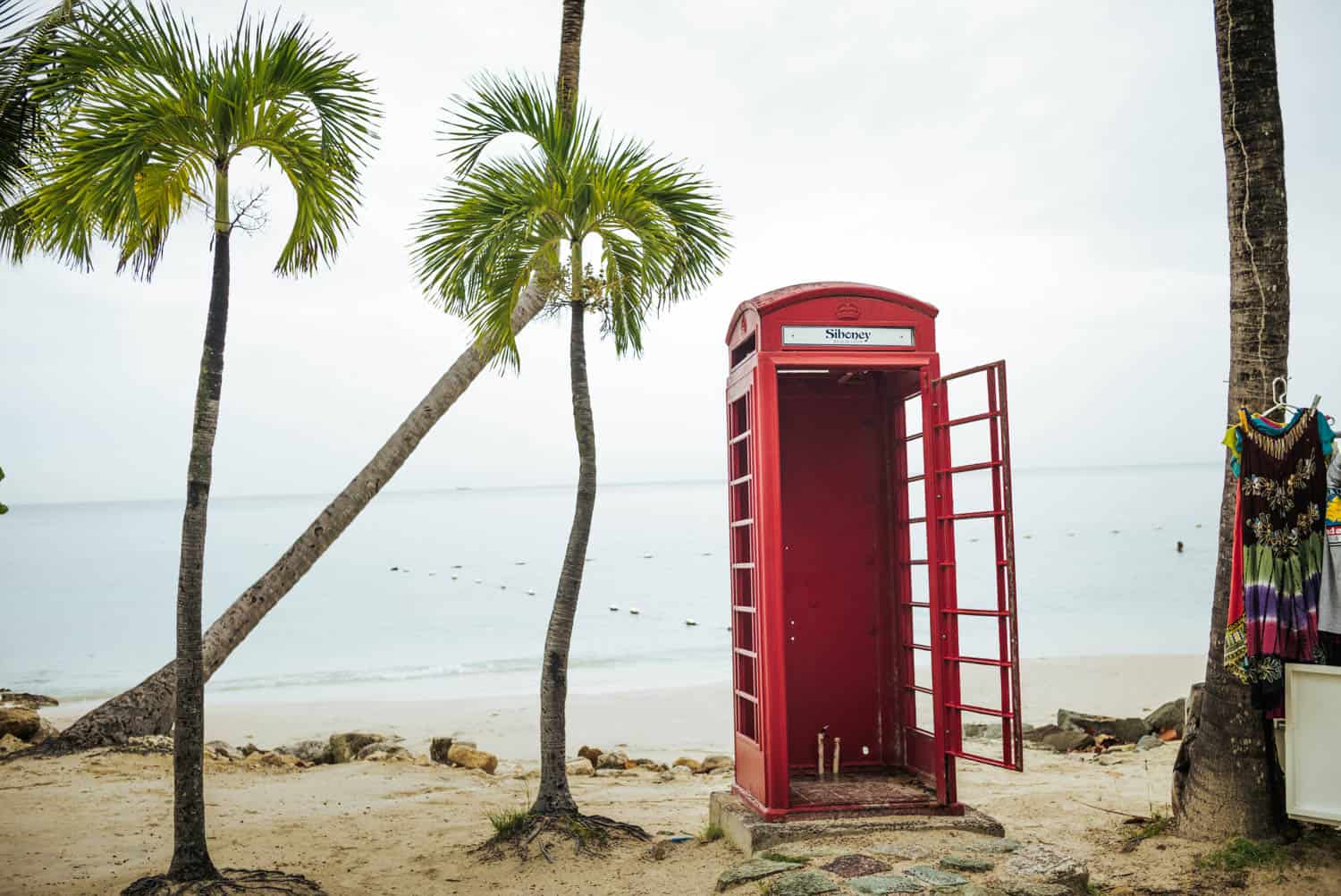 red phone booth in the middle of the beach with palm trees