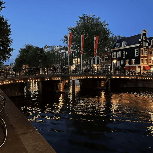 Amsterdam Canal Houses at night over lite bridge with bicycles and trees