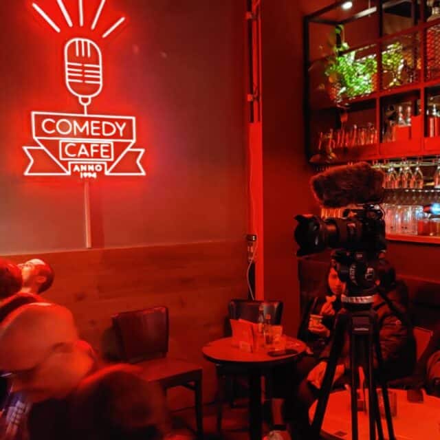 neon red sign showing the Comedy Cafe in text with a microphone and bar