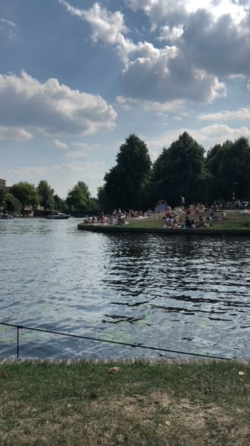 Canal in Erasmuspark with trees and people enjoying the sun sitting on the grass