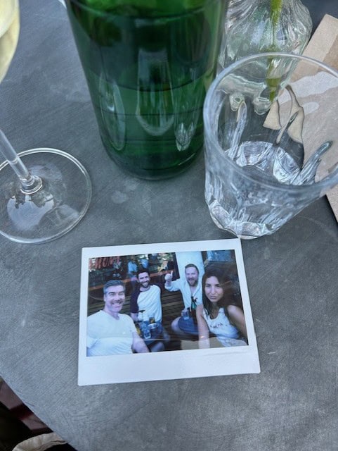 Polaroid picture of four people on a table with glasses