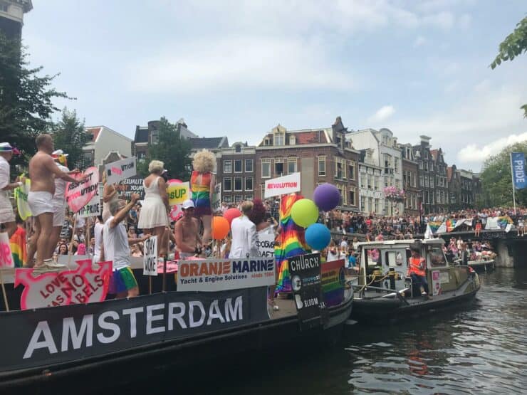 Amsterdam Gay Pride Boat sails down a canal with rainbow covered people