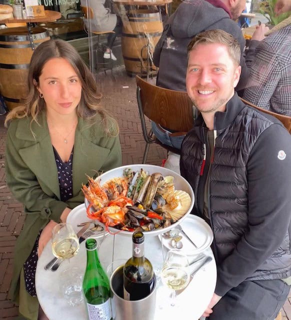 Man and Women smiling with a plate of seafood and a bottle of wine