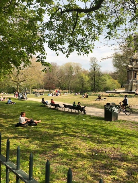 People enjoying Sarphatipark by sitting on a bench, biking, and laying on the grass