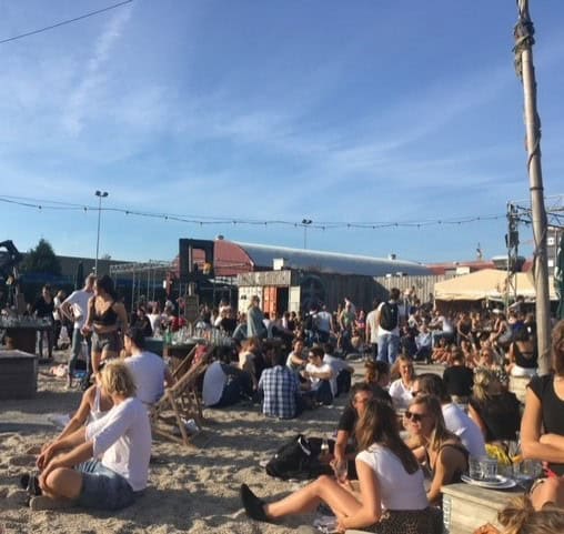 Young people sit in the sand talking at Pllek in Amsterdam