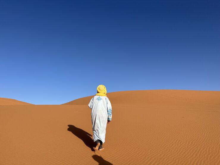 Berber Man walks on a Morocco Desert Tour through the Saharra with golden sand and blue skies