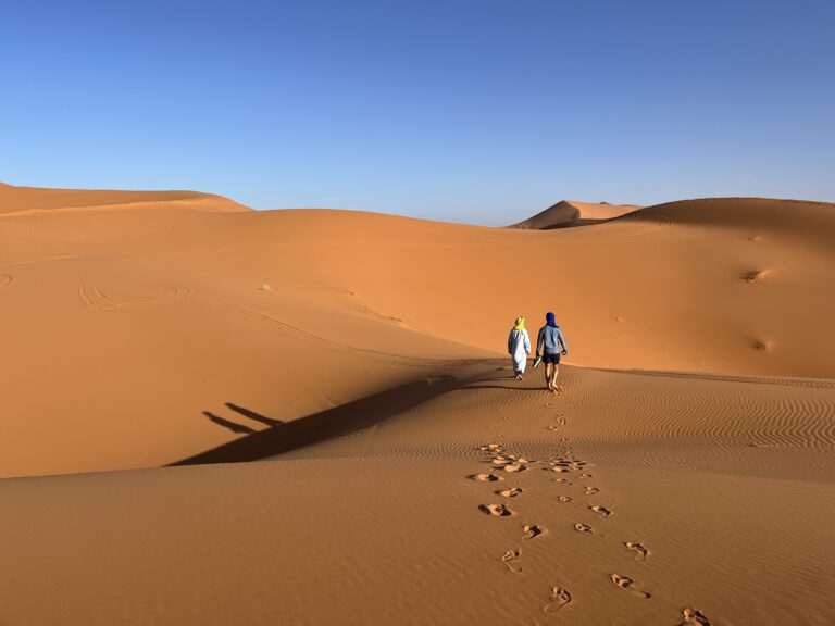 two men walking in the desert with blue skies