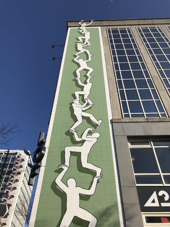 Large street art of people holding each other up and climbing up the building